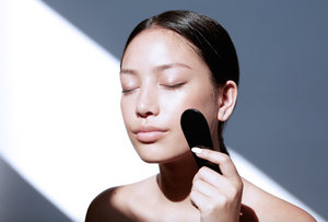 Asian model holding black obsidian gua sha stone tool. Facial massage tool from Traditional Chinese Medicine. 